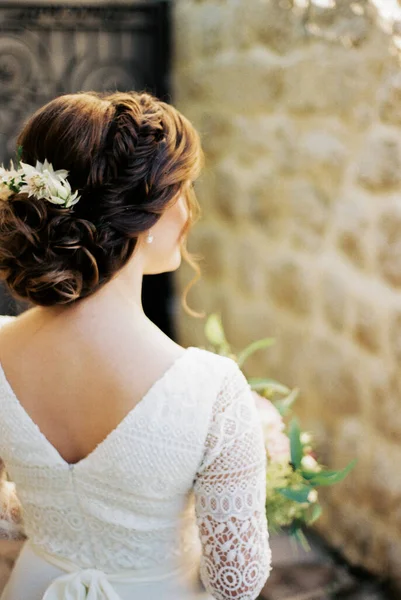 Bride with a beautiful high hairdo is standing in the courtyard of the house. Back view. High quality photo