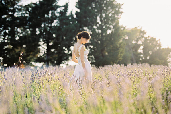 Bride in a white dress stands in a lavender field with her head down. Side view. High quality photo