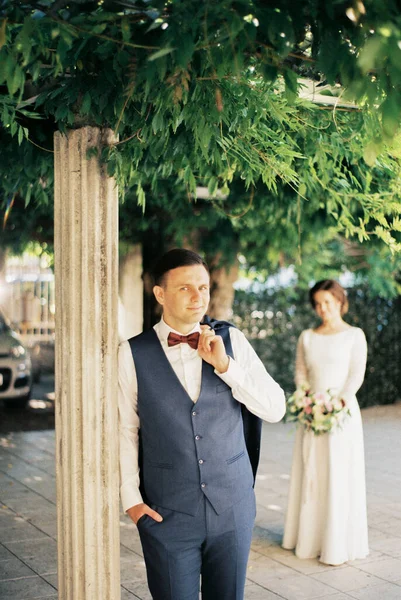 Groom with a jacket on his shoulder leaned against a column in the garden. High quality photo