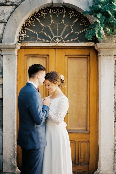 Groom Embrasse Mariée Sur Front Près Une Porte Bois Cintrée — Photo