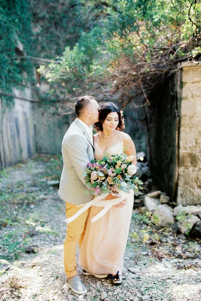 Groom Étreint Mariée Avec Bouquet Près Mur Briques Dans Jardin — Photo