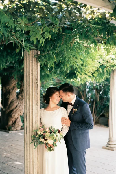 新郎从后面抱着新娘的肩膀 靠近花园的柱子 高质量的照片 — 图库照片