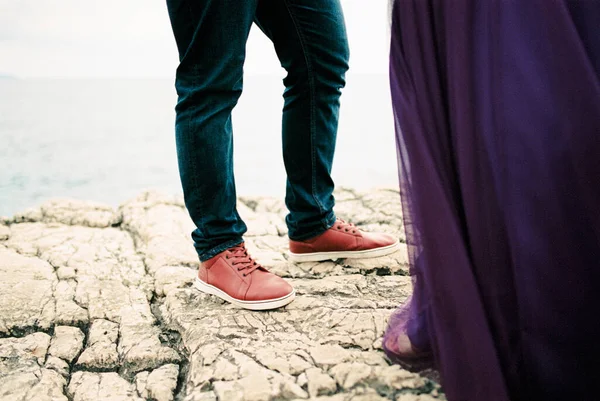 Male and female legs stand on a stone cliff above the sea. Cropped. High quality photo