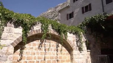 Pencerelerinde panjurları ve sarmaşıkla kaplı tuğla çitleri olan gri taş bir ev. Yüksek kaliteli FullHD görüntüler