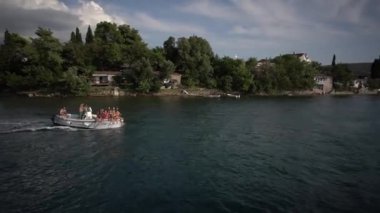 Turistler ellerini sallayarak bir tekneyle kıyıdan geçiyorlar. Yüksek kaliteli FullHD görüntüler