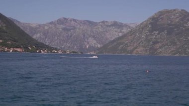 Motorlu tekne hızla bir dağ sırasının arka planına karşı denizde yelken açar. Yüksek kaliteli FullHD görüntüler