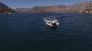 Arka planda bir sıradağ ile denizde seyreden bir motorlu teknenin insansız hava aracı görüntüsü. Yüksek kalite 4k görüntü