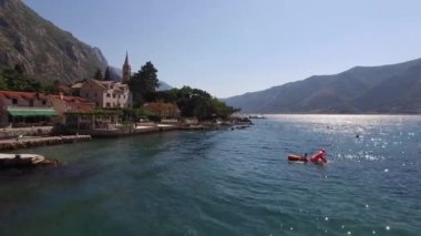Turistler dağların arka planına karşı rıhtıma yakın denizde yüzerler. Yüksek kalite 4k görüntü
