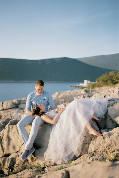 Невеста Лежит Коленях Сидящего Жениха Скалистом Берегу Моря Видом Горы — стоковое фото