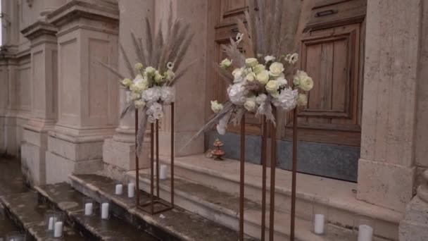 キャンドルスティックのキャンドルは 教会のドアの前に立つ花の花束の横に立っている 高品質のフルHd映像 — ストック動画