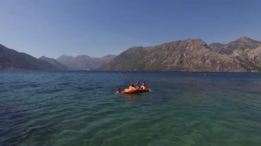 Turistler dağların arka planına karşı denizde şişme bir teknede yüzerler. Yüksek kalite 4k görüntü