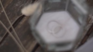 Bir çift alyans, rüzgarda dalgalanan beyaz bir kurdelenin yanındaki cam bir kutuda yatıyor. Yüksek kaliteli FullHD görüntüler