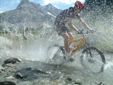 Mountain biker riding through river bed clipart