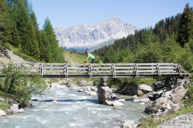 Mountain biker crossing wooden bridge in Swiss mountain area clipart