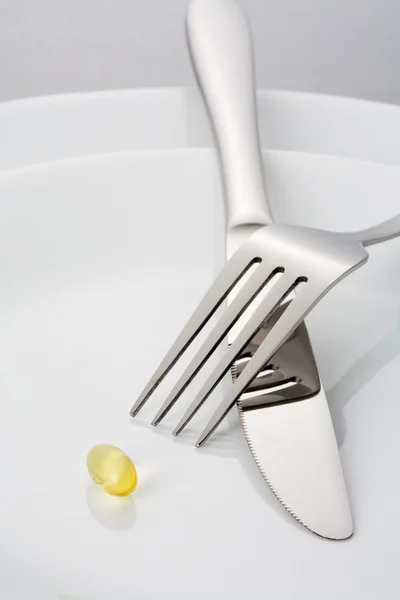 Fourchette, couteau et un seul capsulel d'huile de poisson sur une assiette — Photo