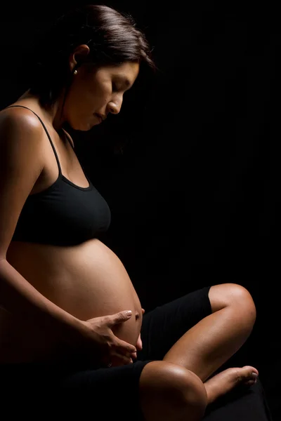 Donna peruviana incinta che si tocca la pancia contro il backgro nero — Foto Stock