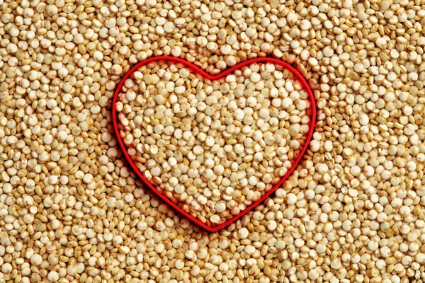 Red heart shape on uncooked quinoa background — Stock Photo, Image