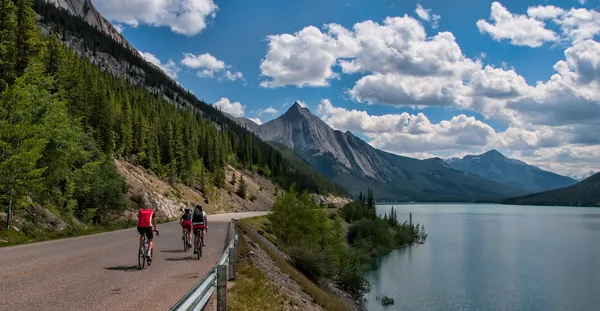 Tre ciclisti su strada con le montagne — Foto Stock