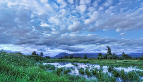 Blauwe landschap met dramatische wolken berg en water — Stockfoto