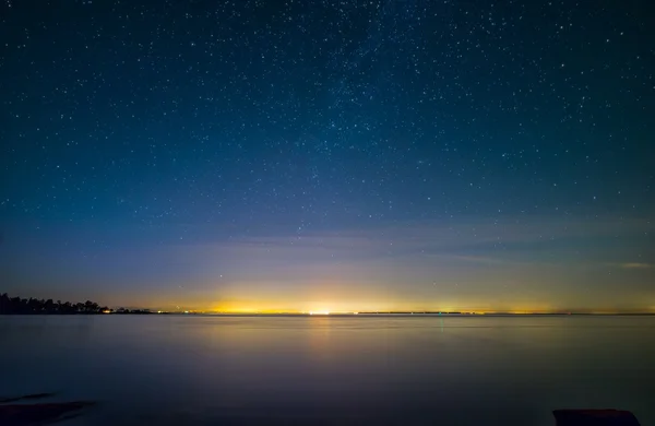 Luzes de cidade distantes com estrelas e água — Fotografia de Stock