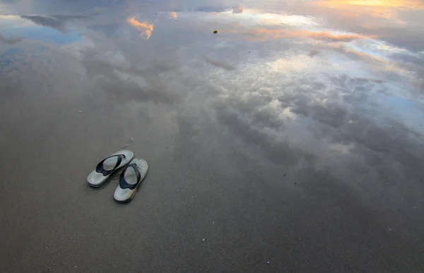 Hausschuhe an einem Sandstrand mit Spiegelung des Sonnenuntergangs — Stockfoto