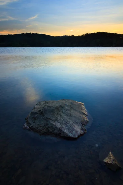 Una roca en el agua con puesta de sol —  Fotos de Stock