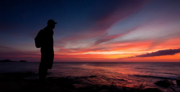 Silhouet van een man die naar de zonsondergang kijkt Stockafbeelding