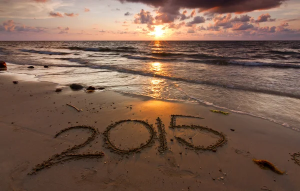 Jaar 2015 geschreven op zand bij zonsondergang Stockafbeelding