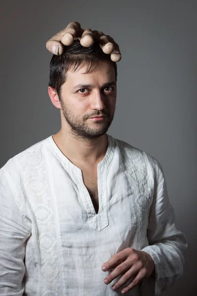 Young bearded man with a huge mock hand on his head — Stock Photo, Image