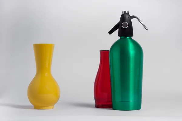 Still life of red bottle yellow vase and green seltzer siphon — Stock Photo, Image