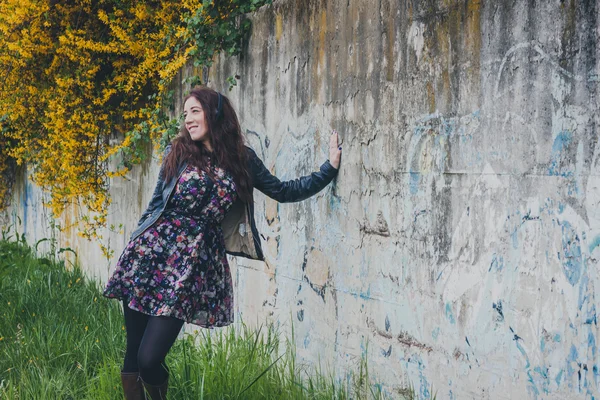 Bella ragazza con i capelli lunghi appoggiata a un muro di cemento — Foto Stock