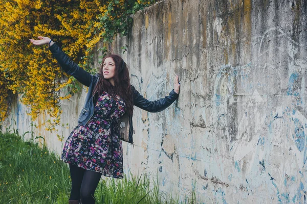 Bella ragazza con i capelli lunghi appoggiata a un muro di cemento — Foto Stock