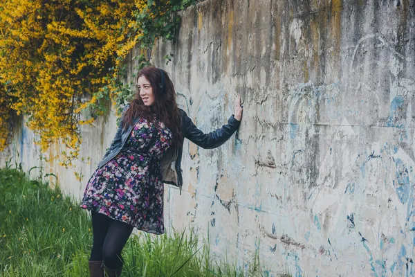 Bella ragazza con i capelli lunghi appoggiata a un muro di cemento — Foto Stock