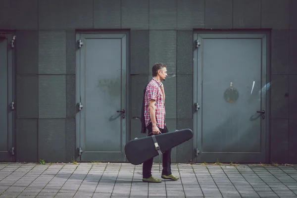 Man in het shirt met korte mouwen wandelen met gitaar koffer — Stockfoto