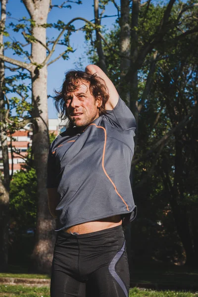 Long haired athlete stretching in a city park — Stock Photo, Image