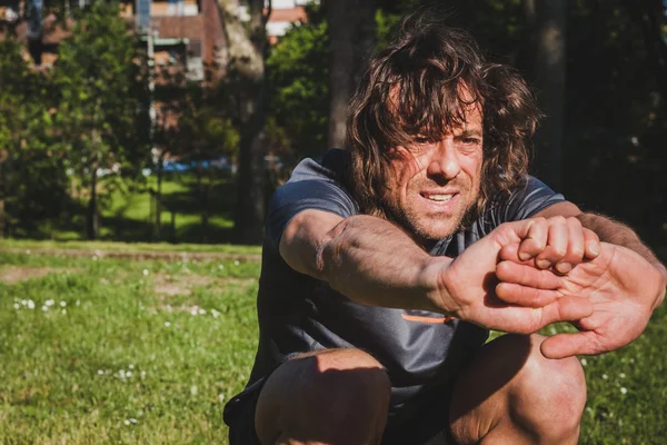 Long haired athlete stretching in a city park — Stock Photo, Image