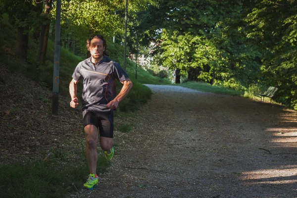 Atleta dai capelli lunghi che corre in un parco cittadino — Foto Stock