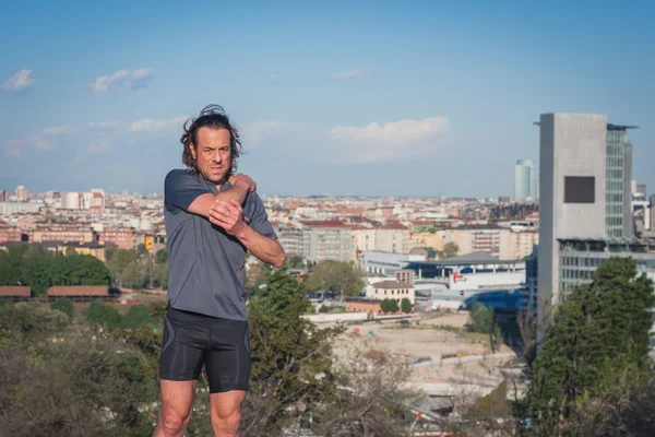 Long haired athlete stretching in a city park — Stock Photo, Image