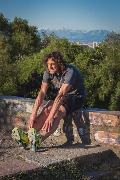 Atleta dai capelli lunghi che si allunga in un parco cittadino — Foto Stock