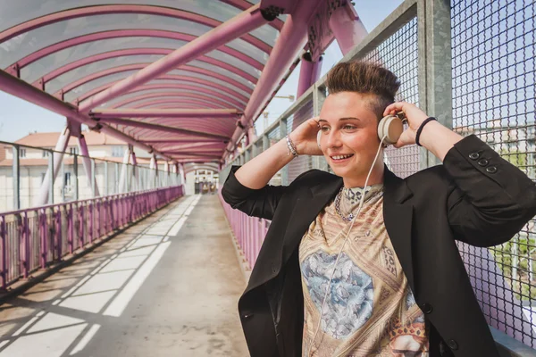 Jolie fille aux cheveux courts écoutant de la musique sur un pont — Photo