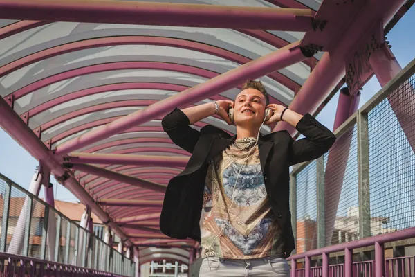 Jolie fille aux cheveux courts écoutant de la musique sur un pont — Photo