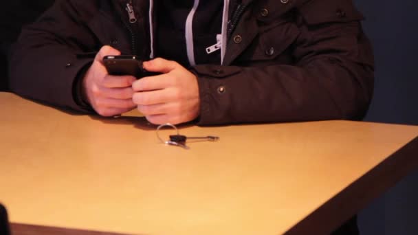 Beelden van de mens aan de tafel zitten en houden van de telefoon — Stockvideo