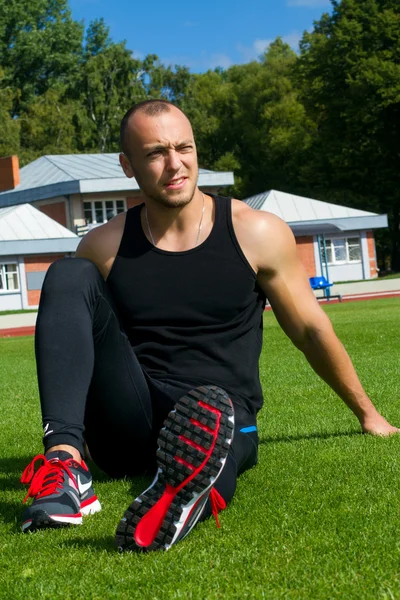 Billede af muskel mand sidder på stadion græs - Stock-foto