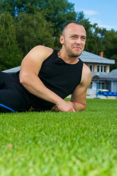 Bilden av muskel man sitter på stadium gräs — Stockfoto