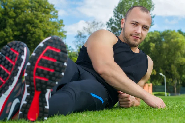 Изображение человека-мышцы, сидящего на траве стадиона — стоковое фото
