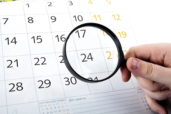 Magnifying glass in hand and the wall calendar — Stock Photo, Image