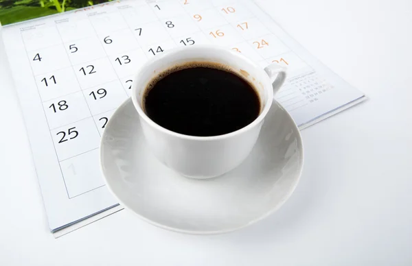 Šálek kávy s nástěnný kalendář na bílém pozadí — Stock fotografie