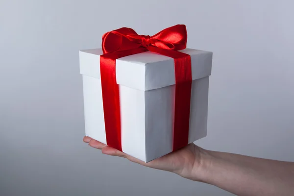 Λευκό δώρο κουτί με κόκκινη κορδέλα στο χέρι — Φωτογραφία Αρχείου