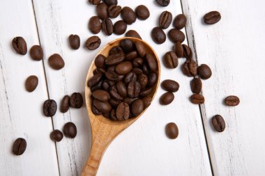 Beyaz ahşap arka planda ahşap kaşıkla kavrulmuş kahve çekirdekleri.