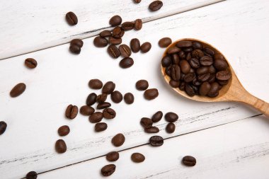 Beyaz ahşap arka planda ahşap kaşıkla kavrulmuş kahve çekirdekleri.